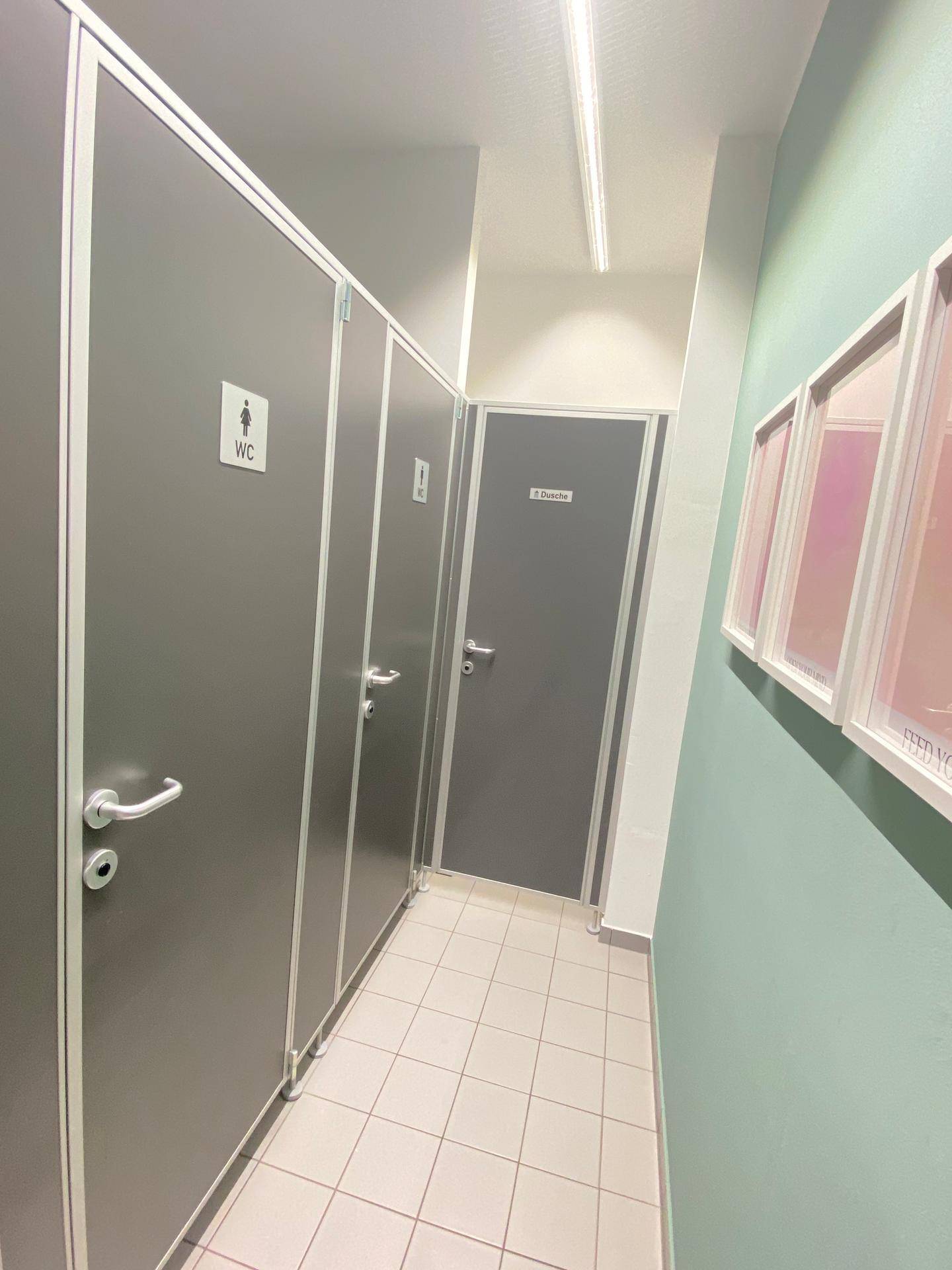 Toilettenbereich mit mehreren Kabinen, Fliesenboden und heller Beleuchtung.