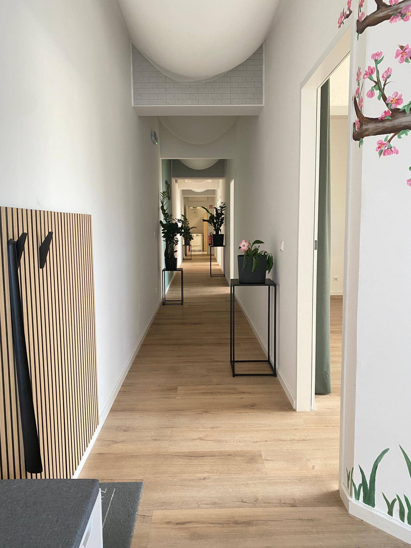 Heller Flur mit Holzlamellenwand, Pflanzen und Türen zu weiteren Räumen.