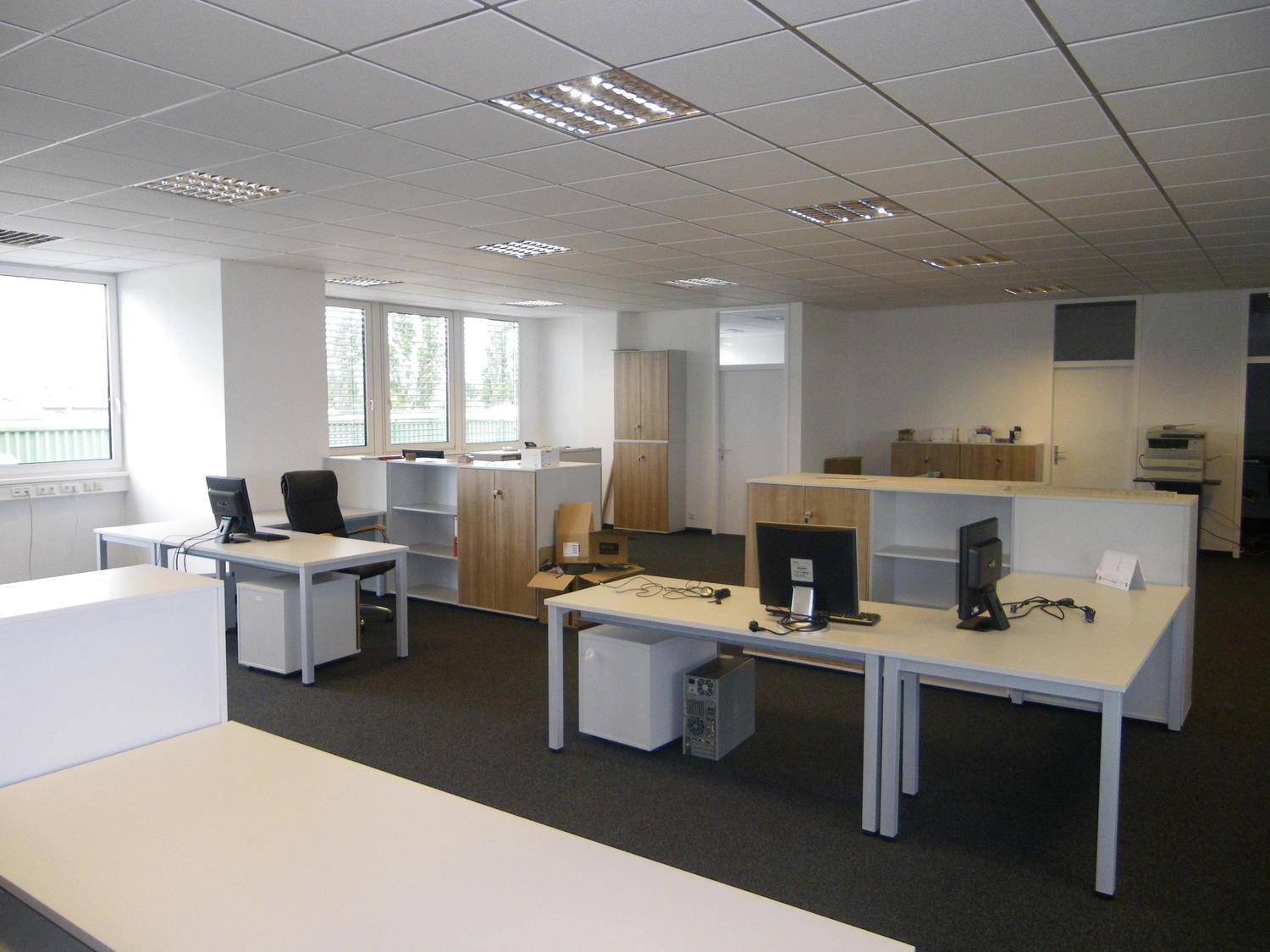 Geräumiges und helles Büro mit mehreren Arbeitsplätzen, Computern und Schränken, ausgestattet mit Teppichboden.