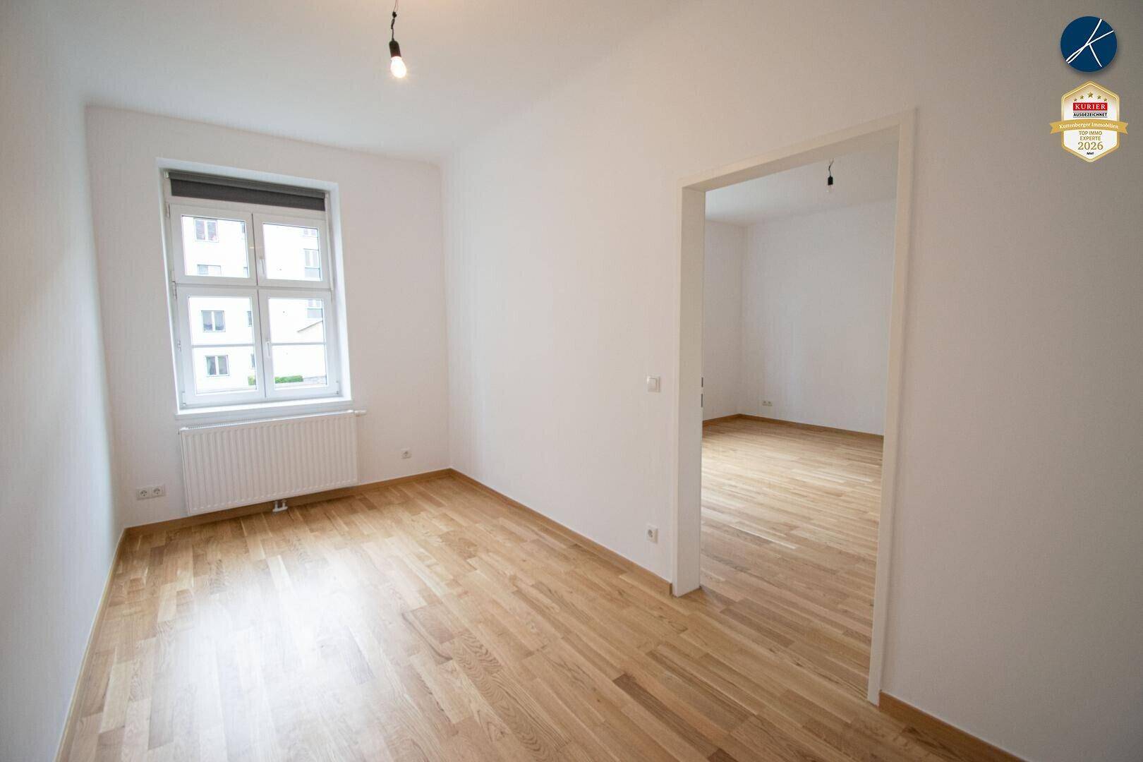 Leerer Wohnraum mit hellem Parkettboden und Fenster, bietet viel Gestaltungspotenzial.