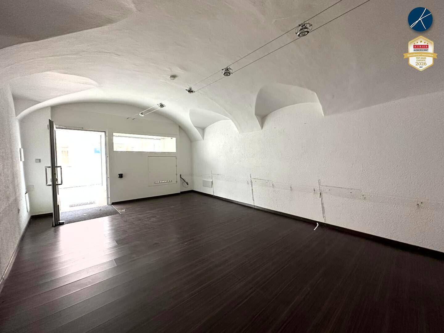 Heller Gewerberaum mit dunklem Holzboden, weißen Wänden und einer beeindruckenden Gewölbedecke, gut beleuchtet durch den Eingang.