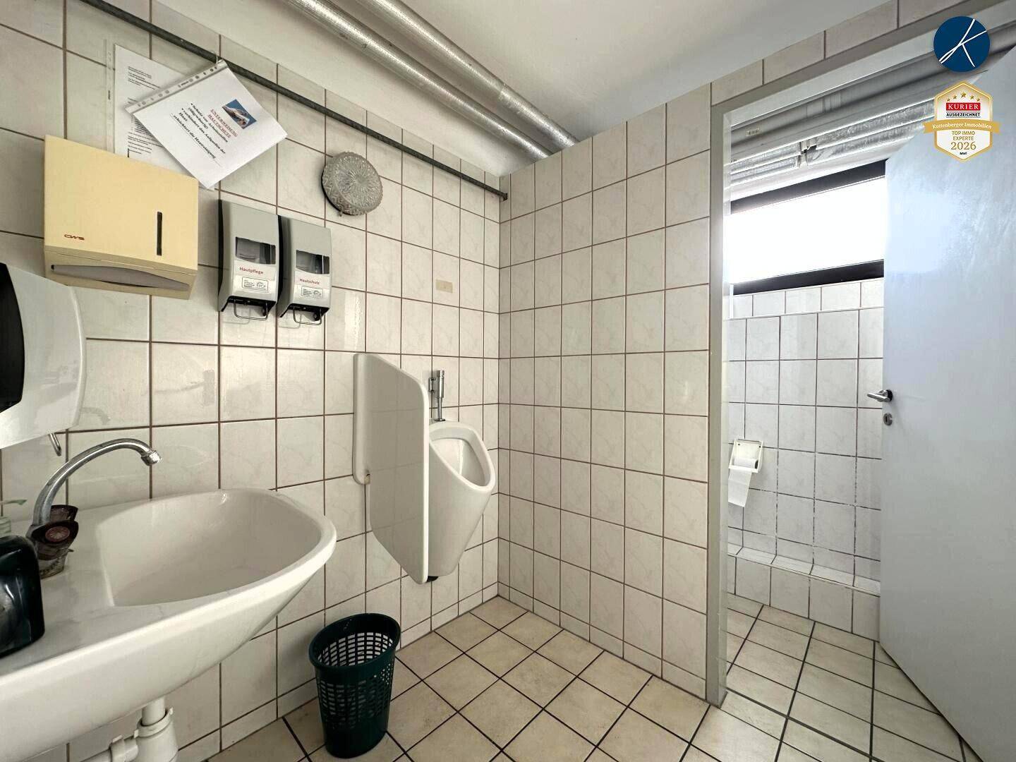 Gefliestes Badezimmer mit Waschbecken und Urinal, sauber und funktional für den gewerblichen Bereich.