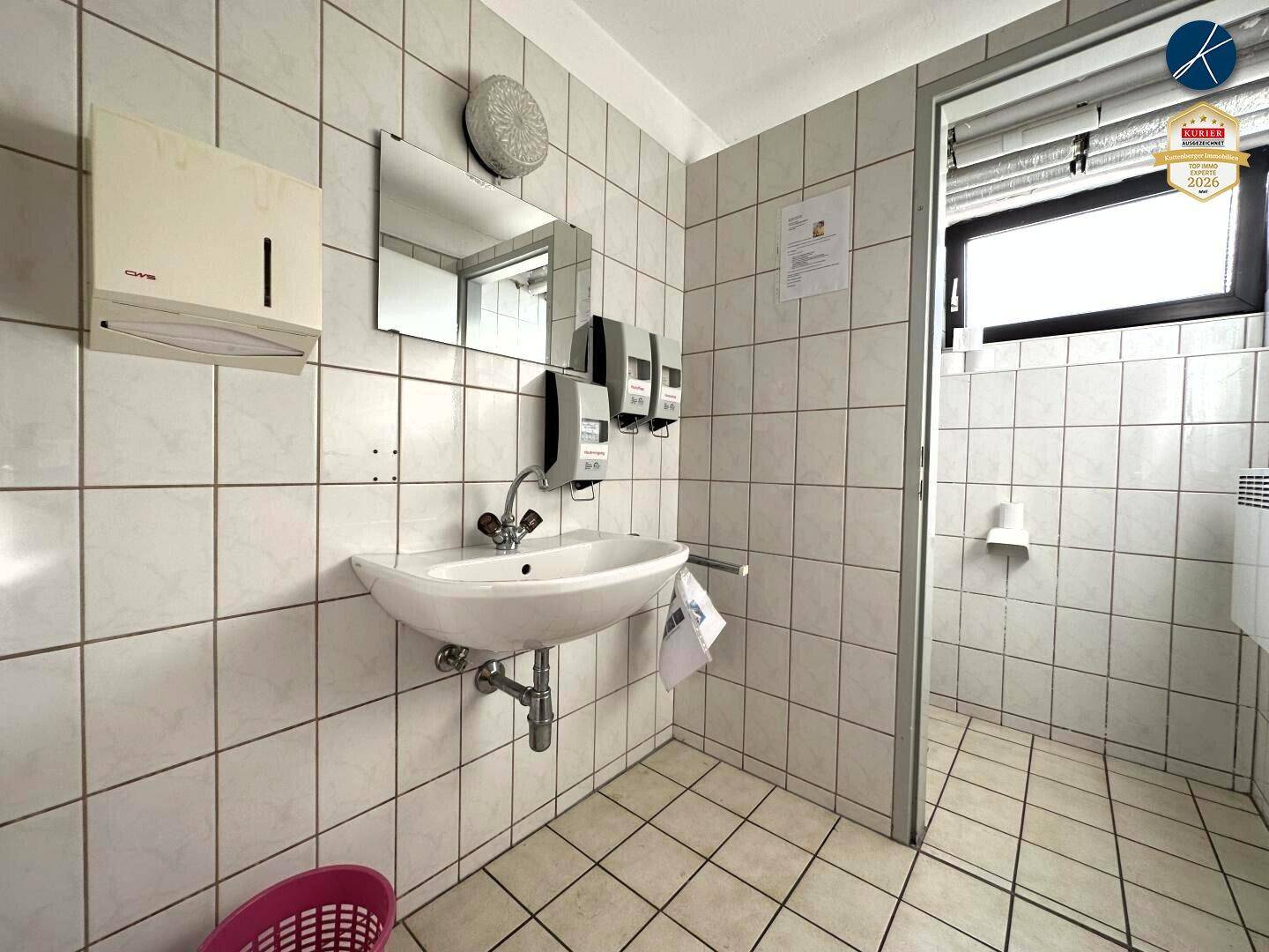 Gefliestes Badezimmer mit Waschbecken, Spiegel und Seifenspender, typisch für gewerbliche Nutzung.