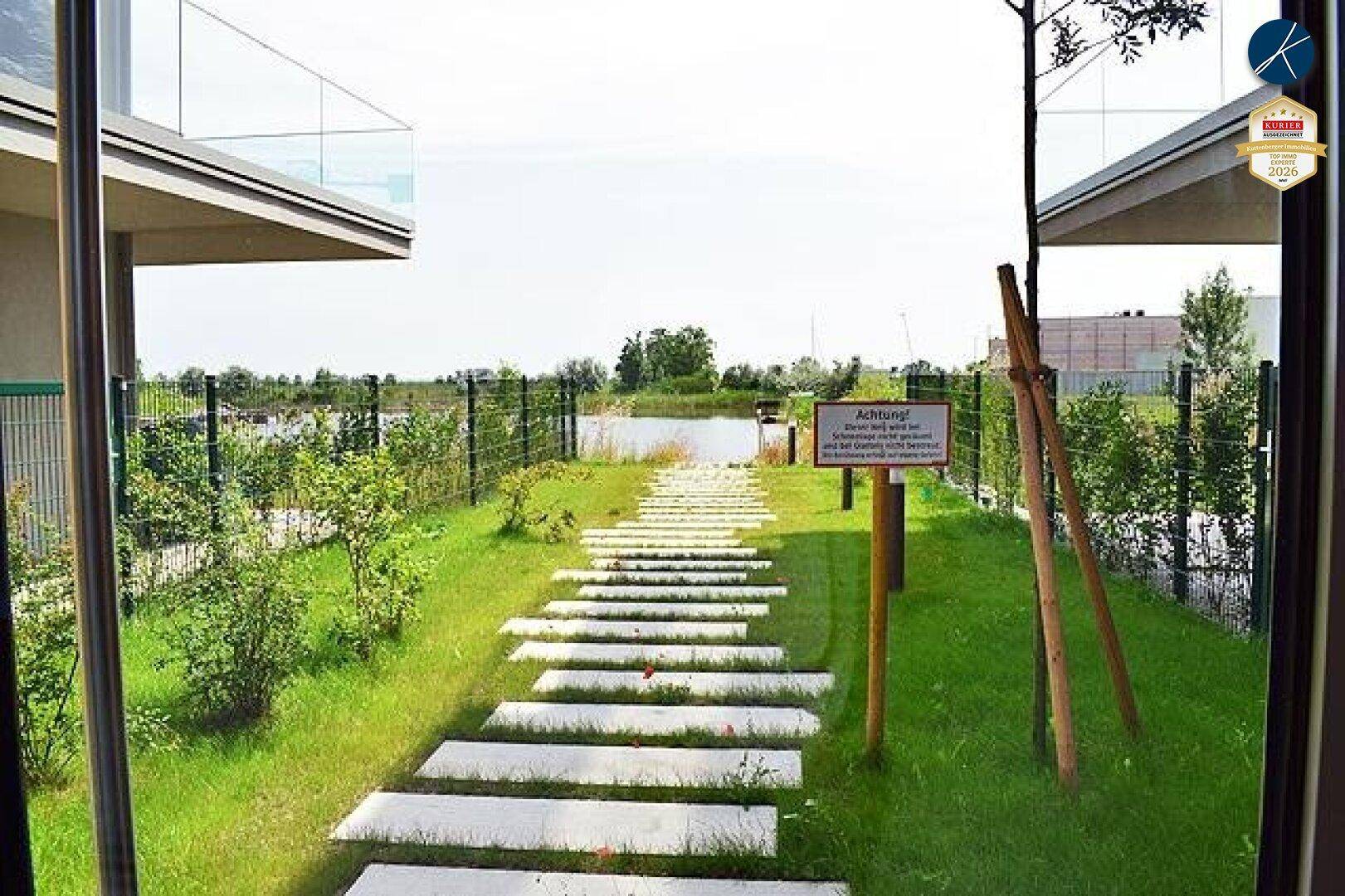 Geschwungener Gartenweg aus Trittplatten führt durch grüne Bepflanzung direkt zum Seeufer.