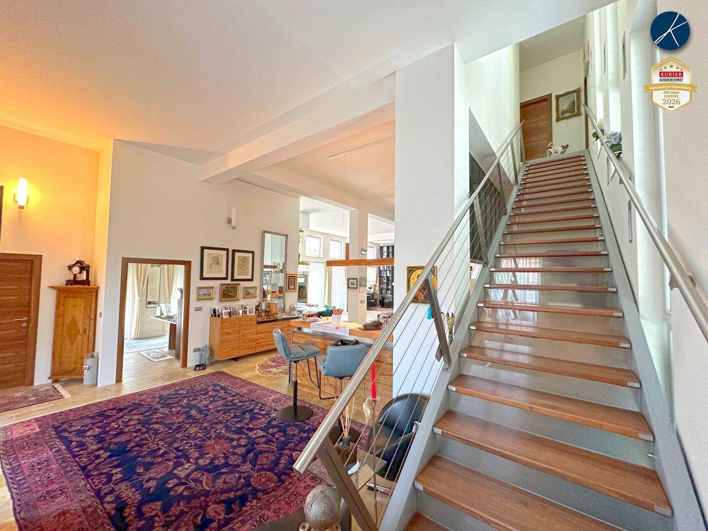Heller Eingangsbereich mit offener Treppe, hohen Decken und Teppichboden.