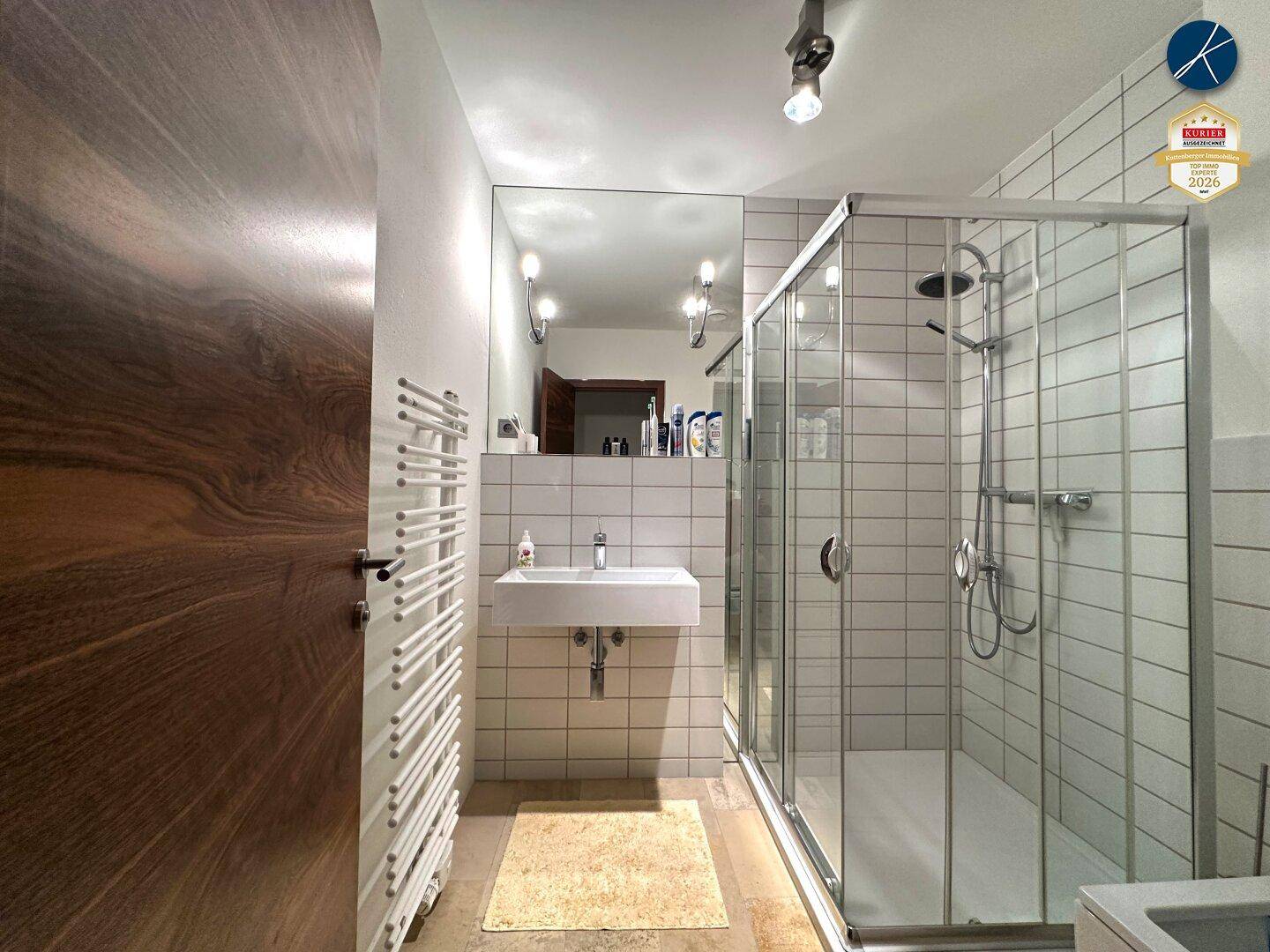 Modernes Badezimmer mit Duschkabine, Waschbecken, großem Spiegel und Handtuchheizkörper.