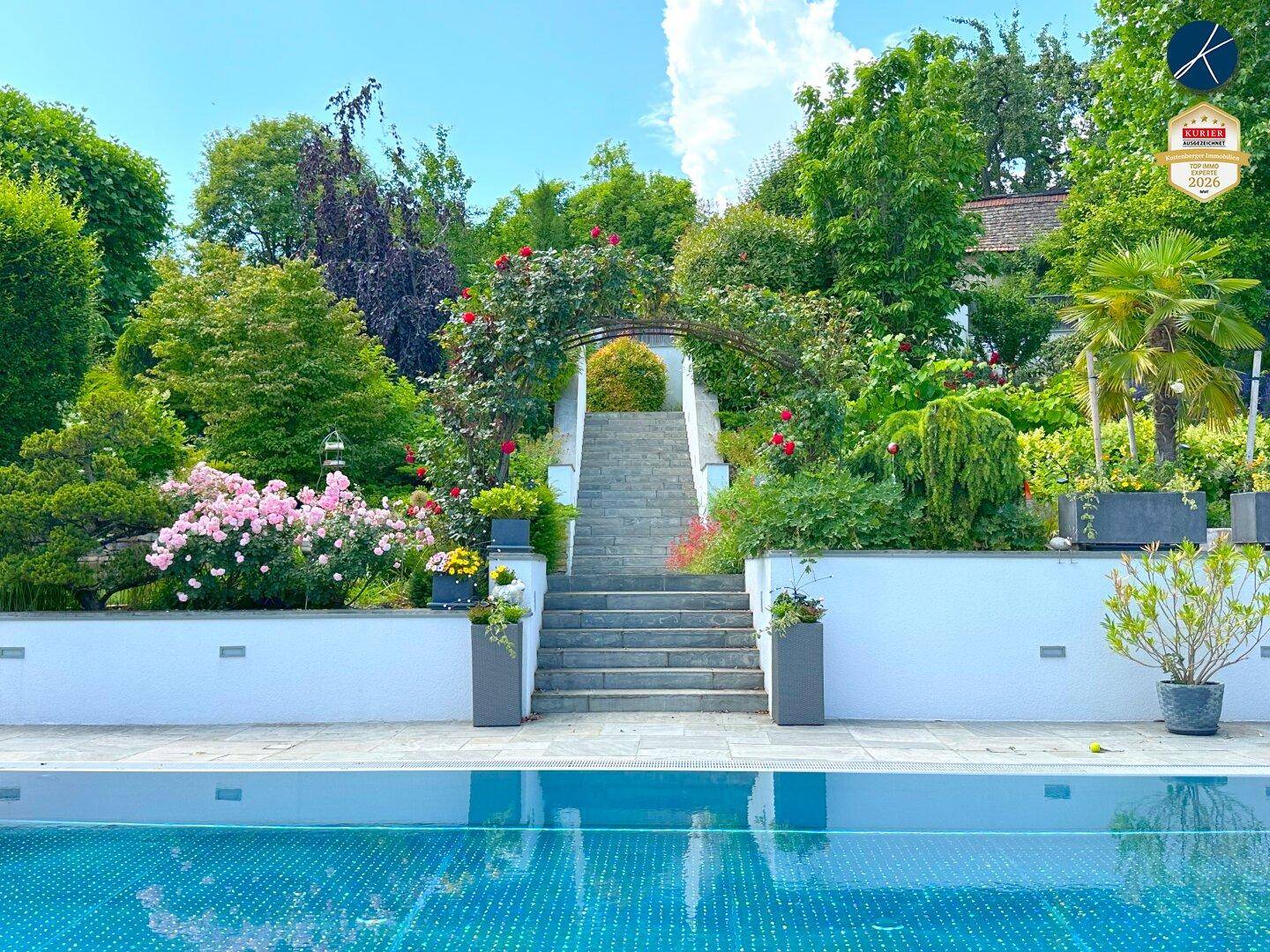 Üppiger Gartenbereich mit Steintreppe, blühenden Pflanzen und Blick auf den Pool.