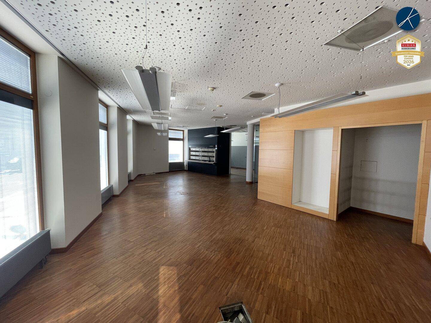Großer, leerer Büroraum mit Holzparkettboden, Akustikdecke und breiten Fenstern, ideal für flexible Nutzung.