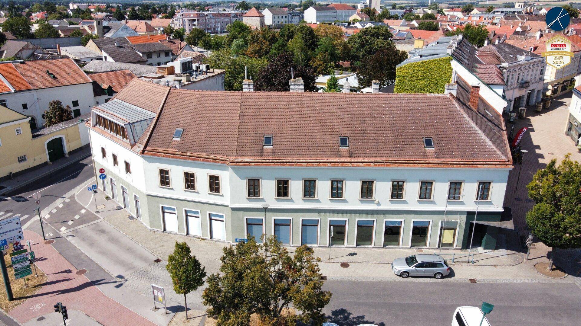 Luftaufnahme eines großen Gebäudes mit braunem Ziegeldach und vielen Fenstern in einer städtischen Umgebung.