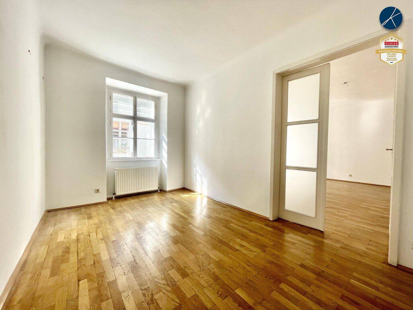Gemütliches Zimmer mit Holzboden und einem großen Fenster, das den Raum mit natürlichem Licht erfüllt.