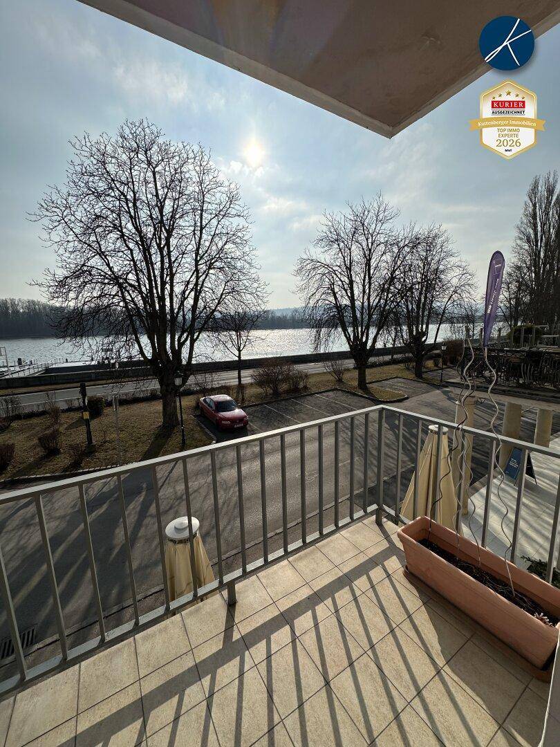 Ein sonniger Balkon mit Fliesenboden und Blick auf einen Fluss und Bäume.