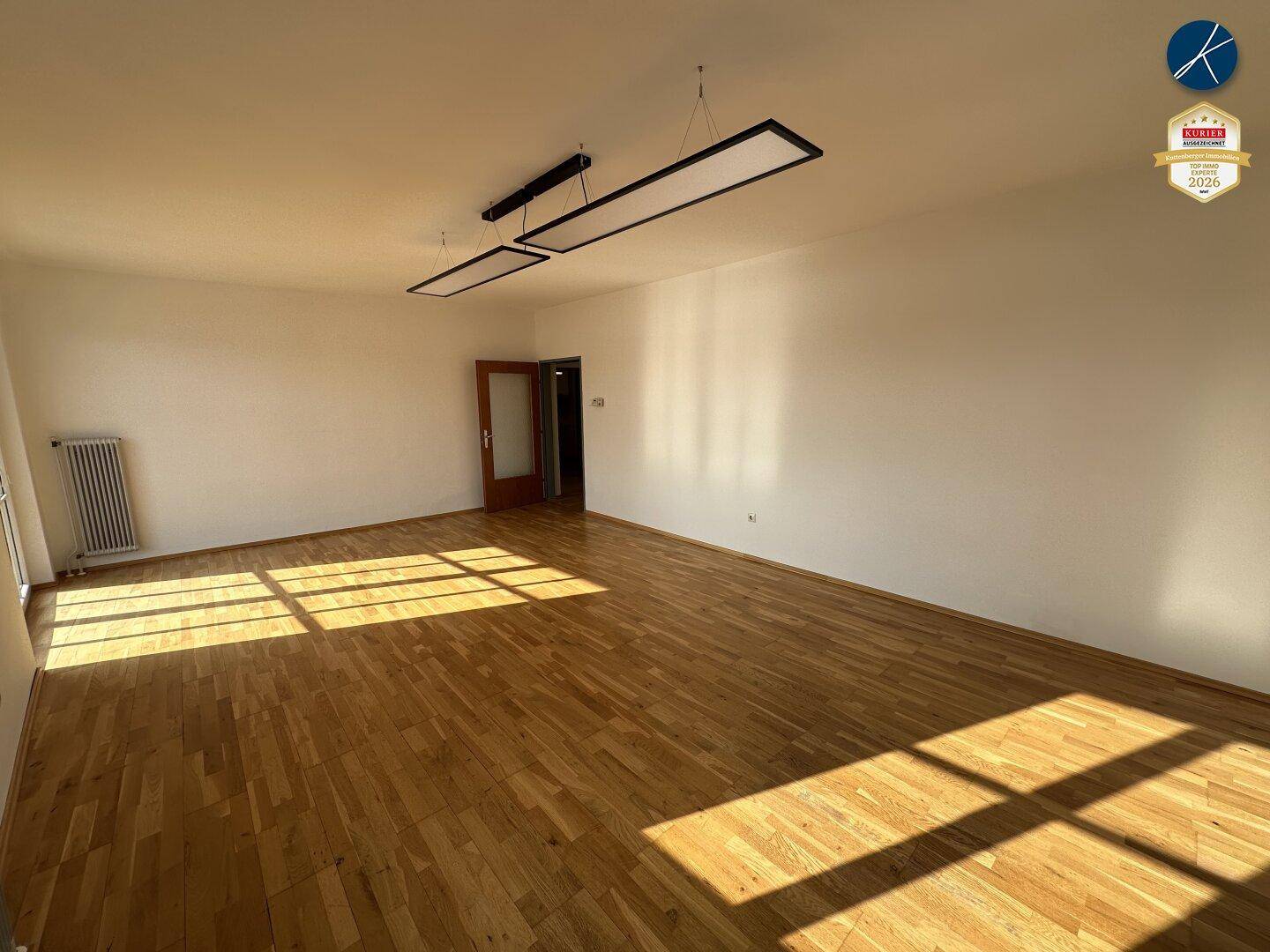 Leerer Büroraum mit Holzboden und weißen Wänden, durchflutet von natürlichem Sonnenlicht.