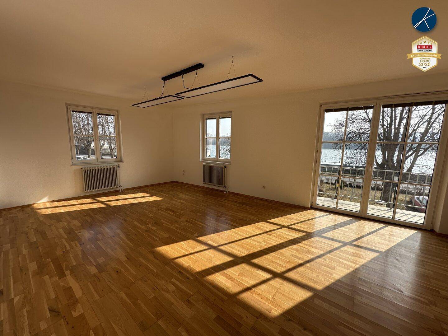 Geräumiger, unmöblierter Büroraum mit Holzboden und großen Fenstern, die viel Tageslicht hereinlassen.