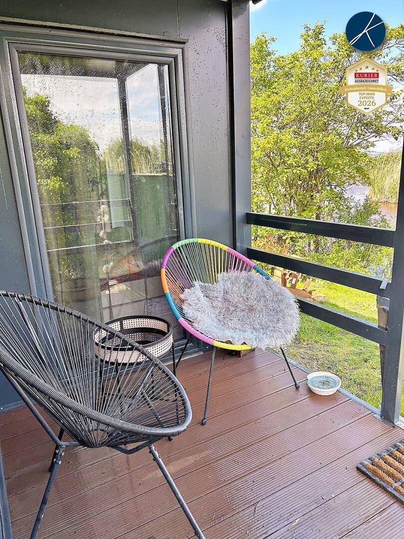 Kleiner Balkon mit bunten Stühlen und Blick ins Grüne sowie auf das nahegelegene Wasser.
