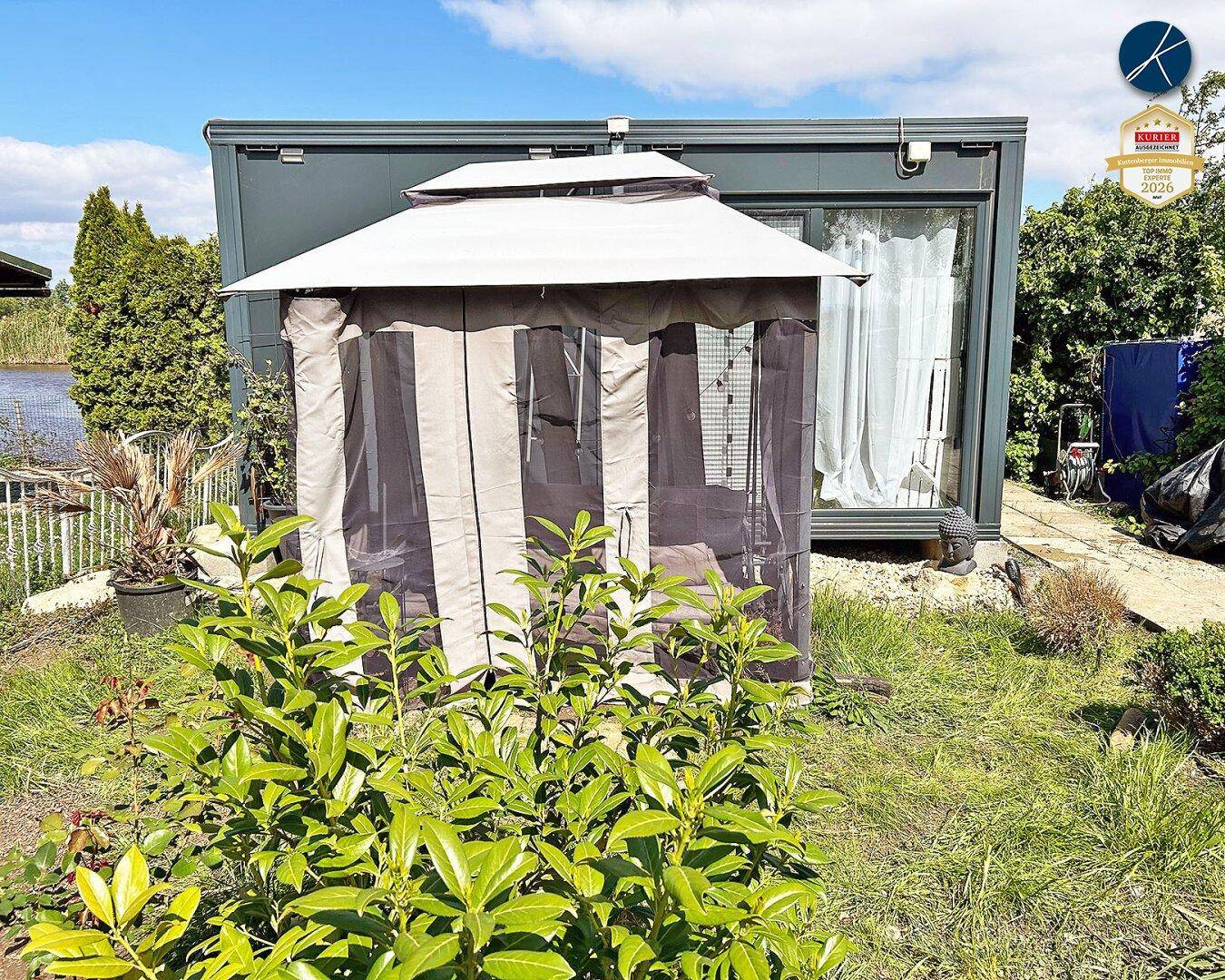 Gartenbereich vor einem modernen Gebäude mit einem Pavillon und grüner Bepflanzung.