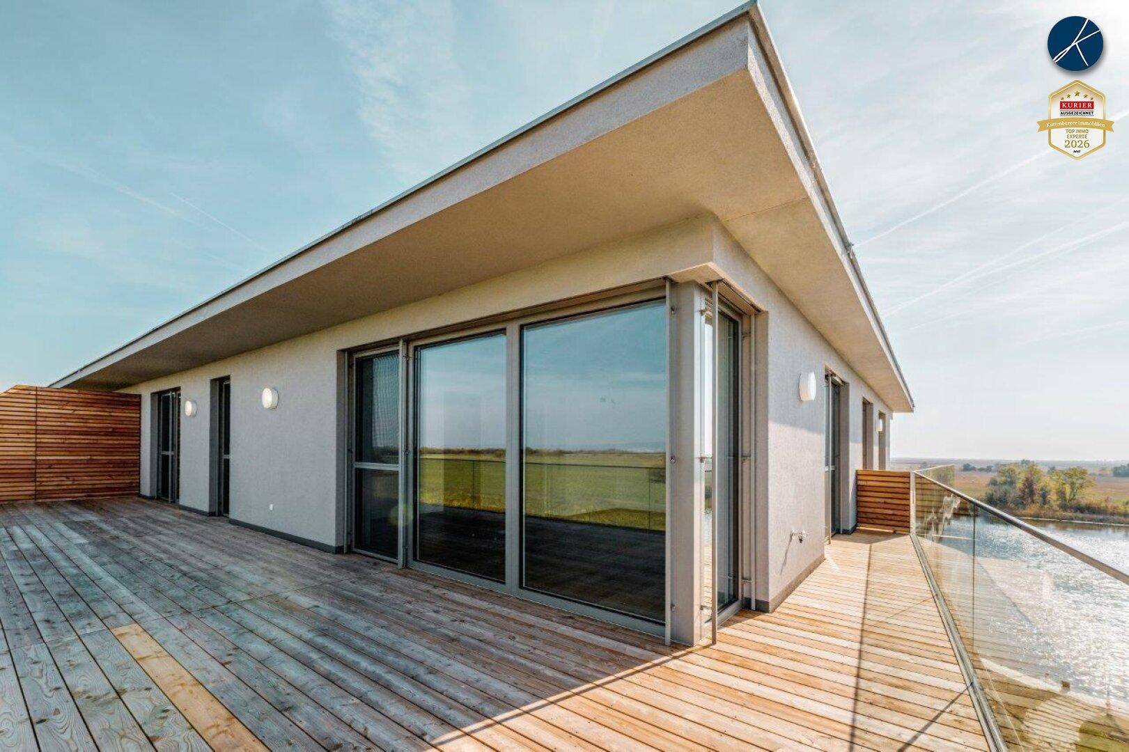 Geräumige Holzterrasse mit Glasgeländer und weitem Blick über die Landschaft und den See.