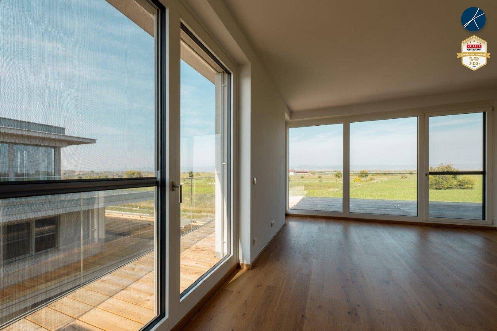 Lichtdurchflutetes Wohnzimmer mit weitem Blick über die grüne Landschaft durch bodentiefe Fenster.