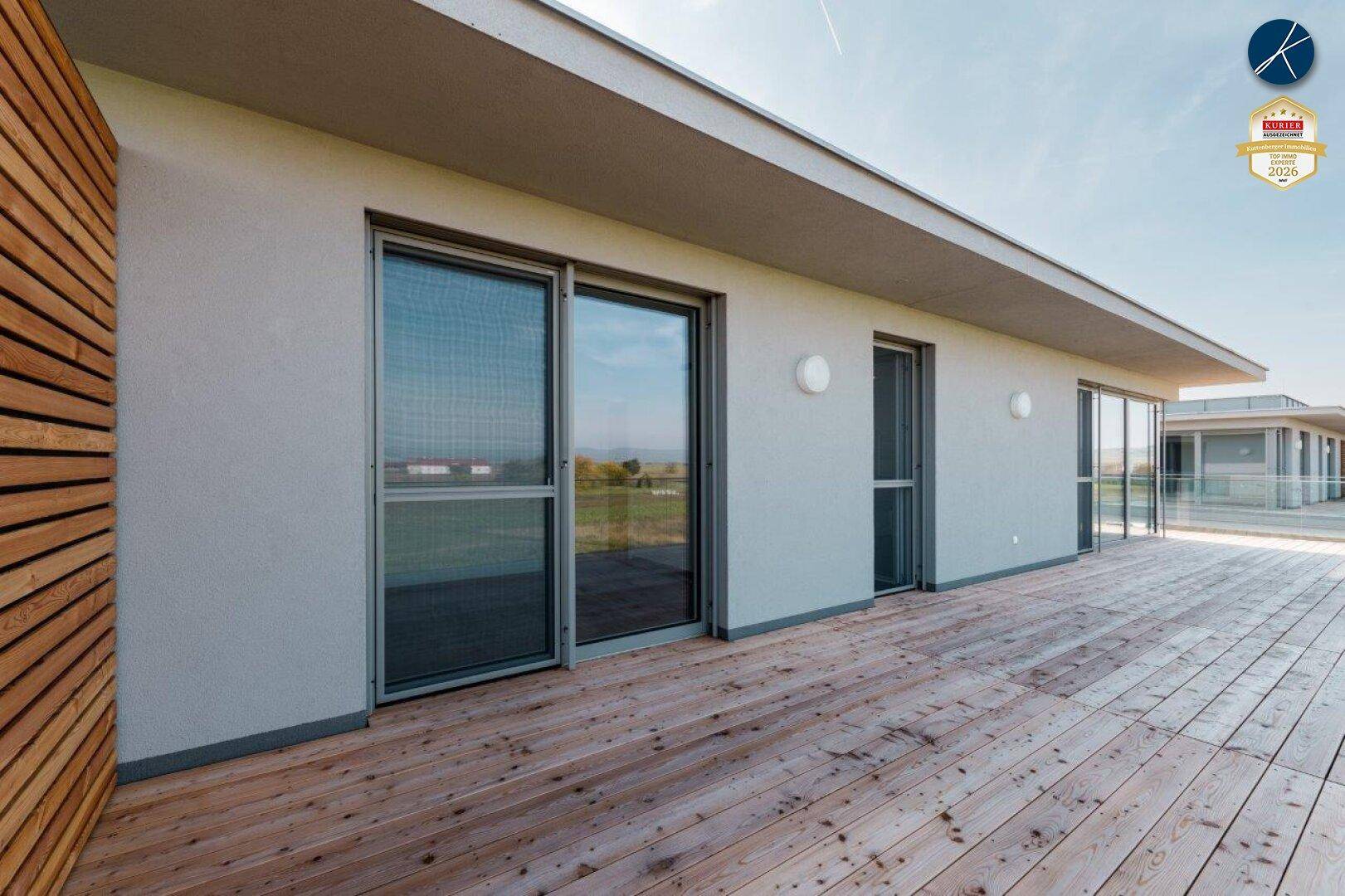 Weitläufige Holzterrasse mit Schiebetüren und Blick auf die umliegende Natur und den See.