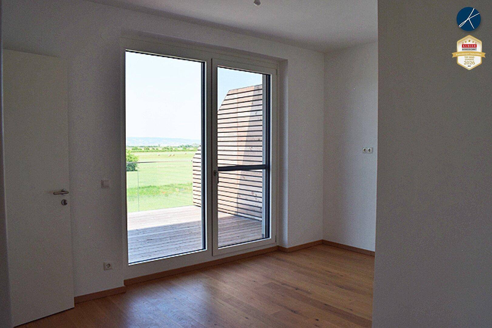 Helles Schlafzimmer mit Holzboden und Zugang zu einem Balkon mit Blick ins Grüne.