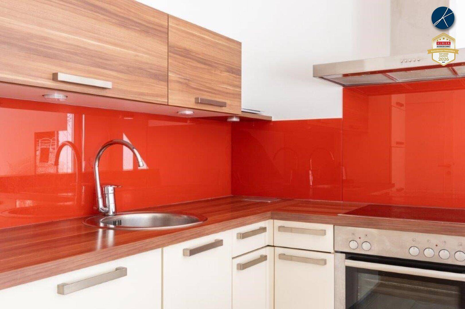 Moderne Einbauküche mit Holzfronten, roter Glasrückwand und Edelstahlspüle.