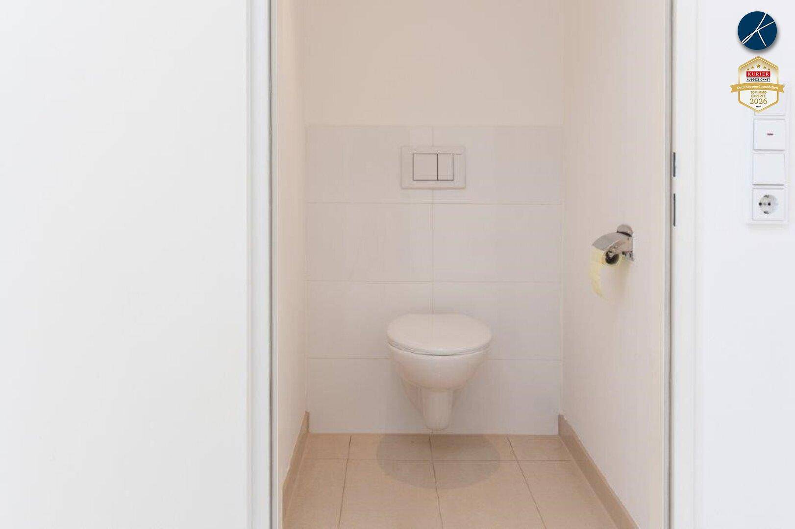 Separates WC mit wandhängender Toilette und hellen Fliesen an Wänden und Boden.