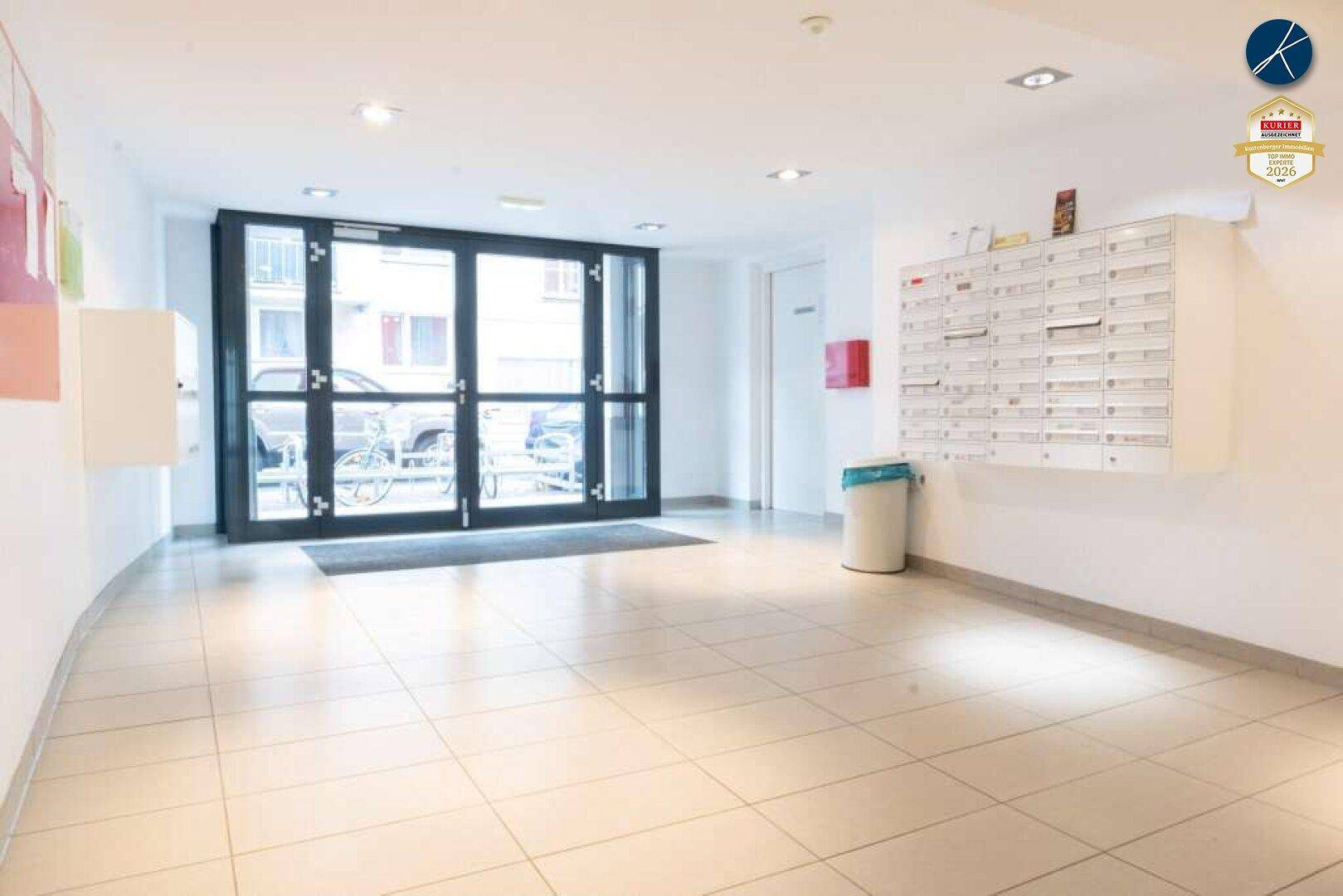 Heller Eingangsbereich eines Mehrfamilienhauses mit Briefkästen und großen Glastüren.