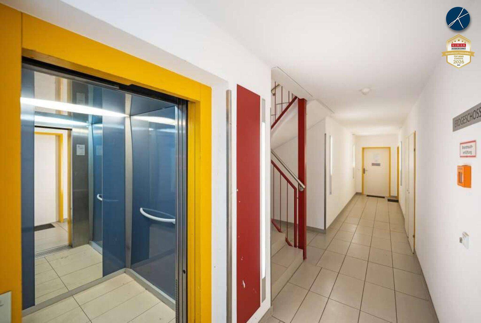 Flur im Mehrfamilienhaus mit Aufzug, Treppenhaus und gefliestem Boden.
