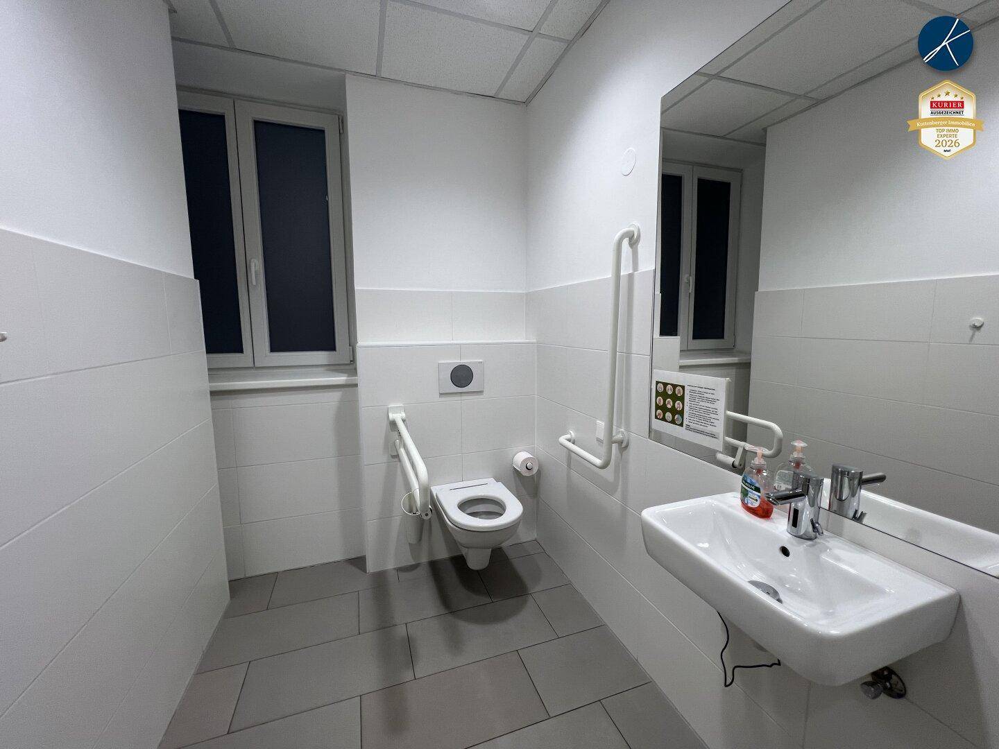 Barrierefreies Badezimmer mit Haltegriffen, wandhängendem WC und großem Spiegel.