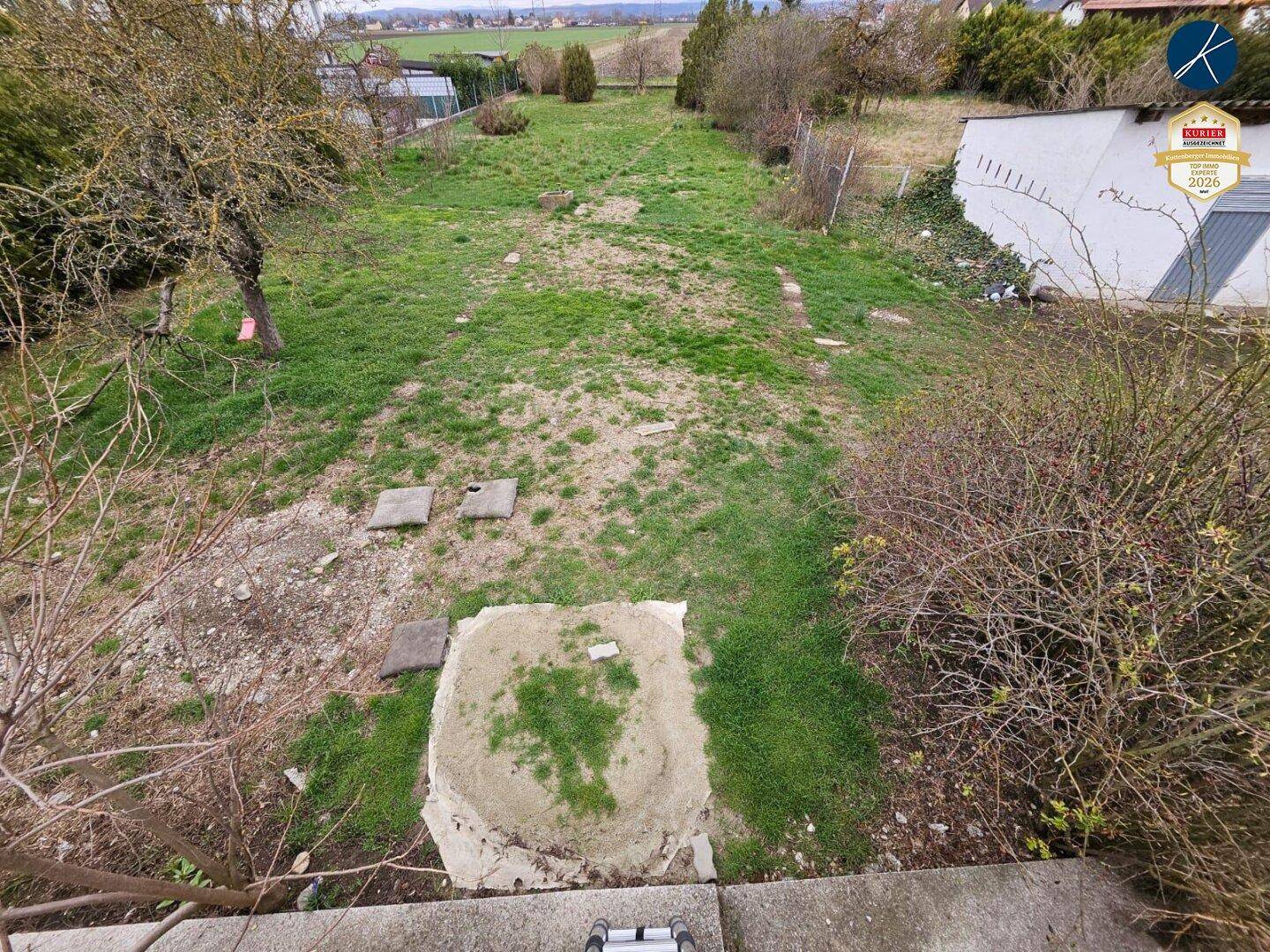 Unbebautes Gartengrundstück mit Blick auf die umliegende Landschaft und einige Bäume.
