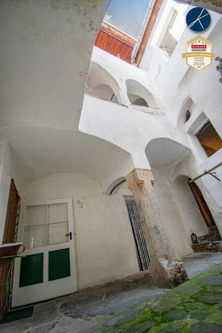 Historischer Innenhof mit weißen Arkaden, Steinboden und einer traditionellen grün-weißen Tür.