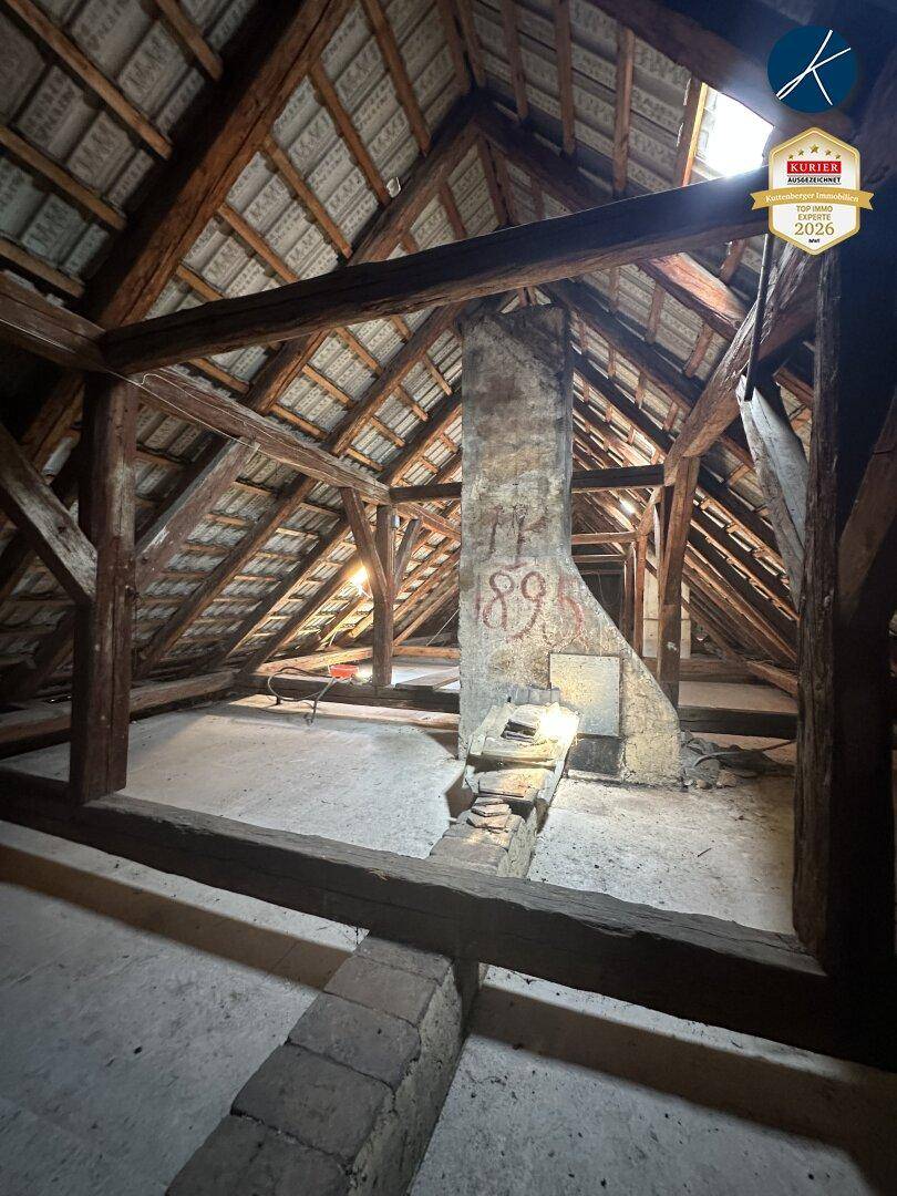 Historischer Dachboden mit freiliegenden Holzbalken und einem alten Schornstein, ideal für Renovierung.