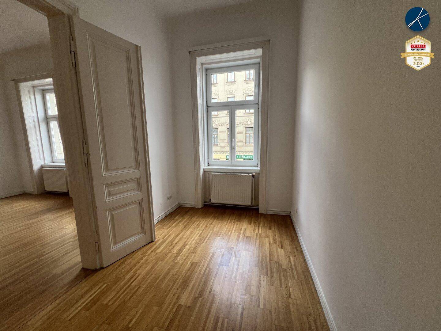 Helles Zimmer mit Parkettboden und einem Fenster, das viel Tageslicht hereinlässt.