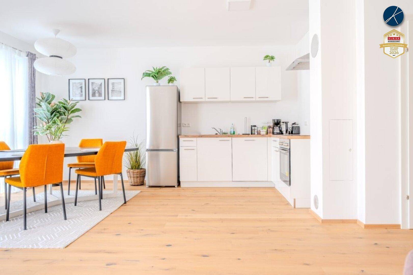 Moderne weiße Einbauküche mit Edelstahlofen und Kühlschrank im offenen Wohnbereich.