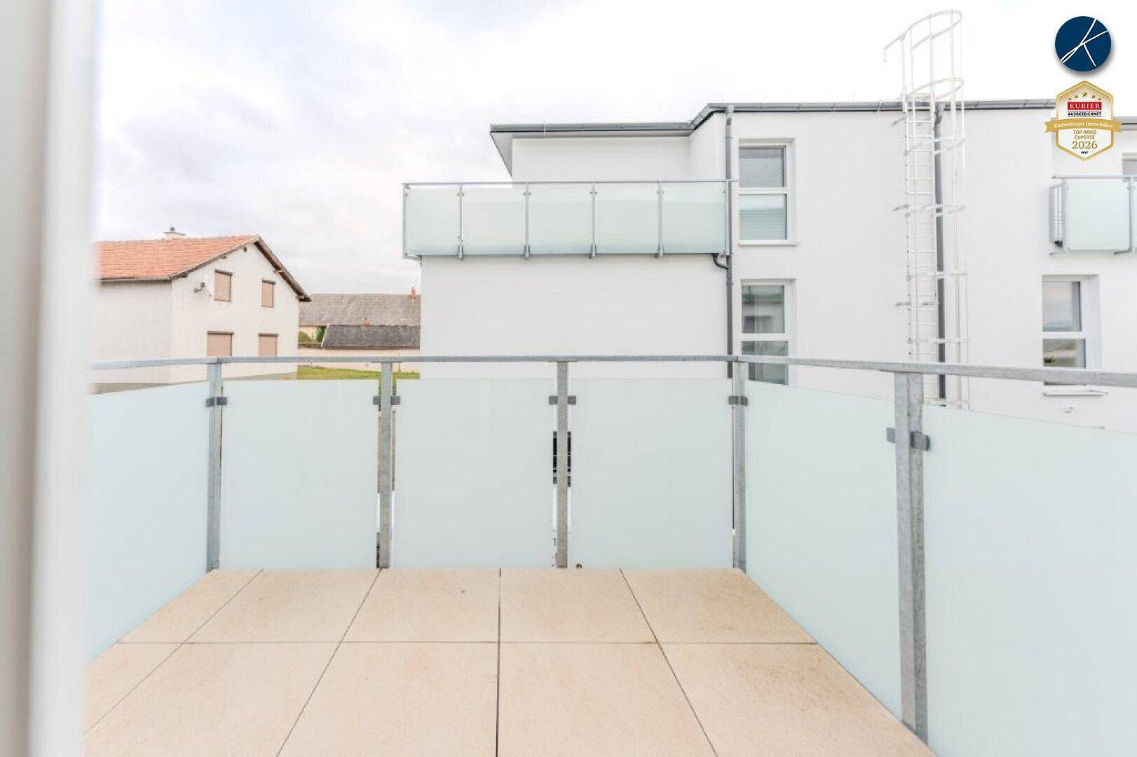 Moderner Balkon mit Glasbrüstung und Fliesenboden, bietet einen Blick auf die Umgebung.
