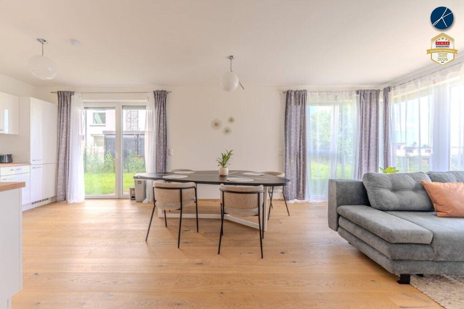 Offener Wohn- und Essbereich mit Holzboden, großem Sofa und Zugang zum Garten.