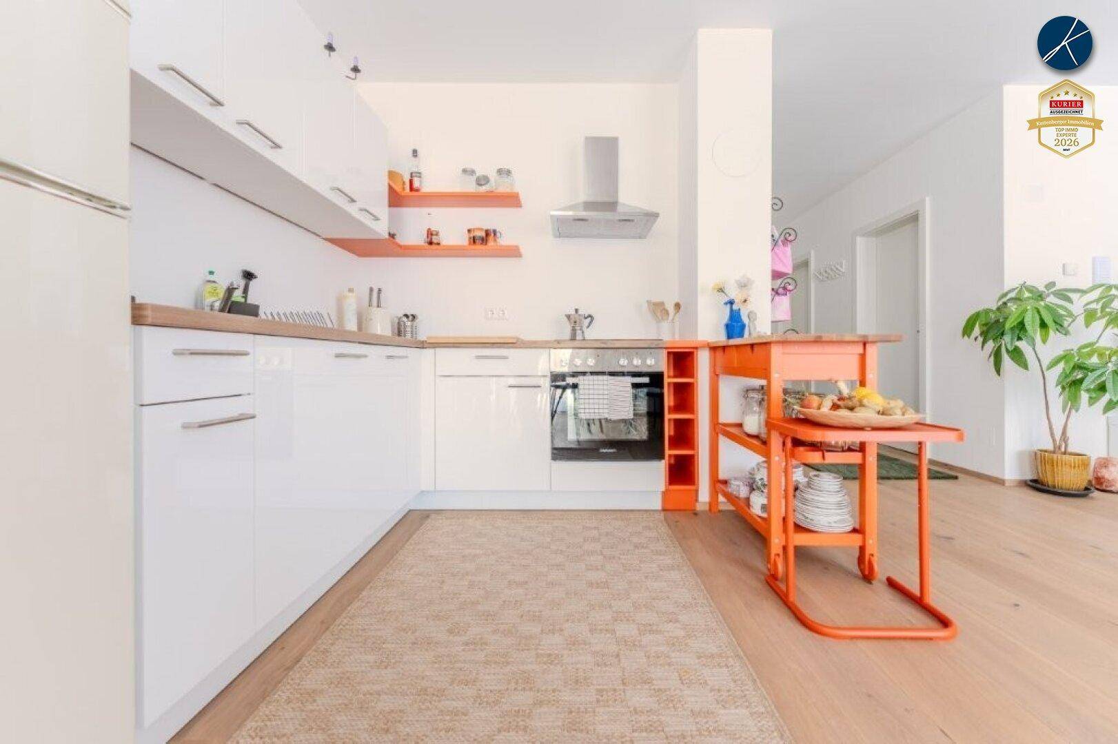 Moderne Küche mit weißen Hochglanzschränken, Holzarbeitsplatte und einem auffälligen orangefarbenen Servierwagen.