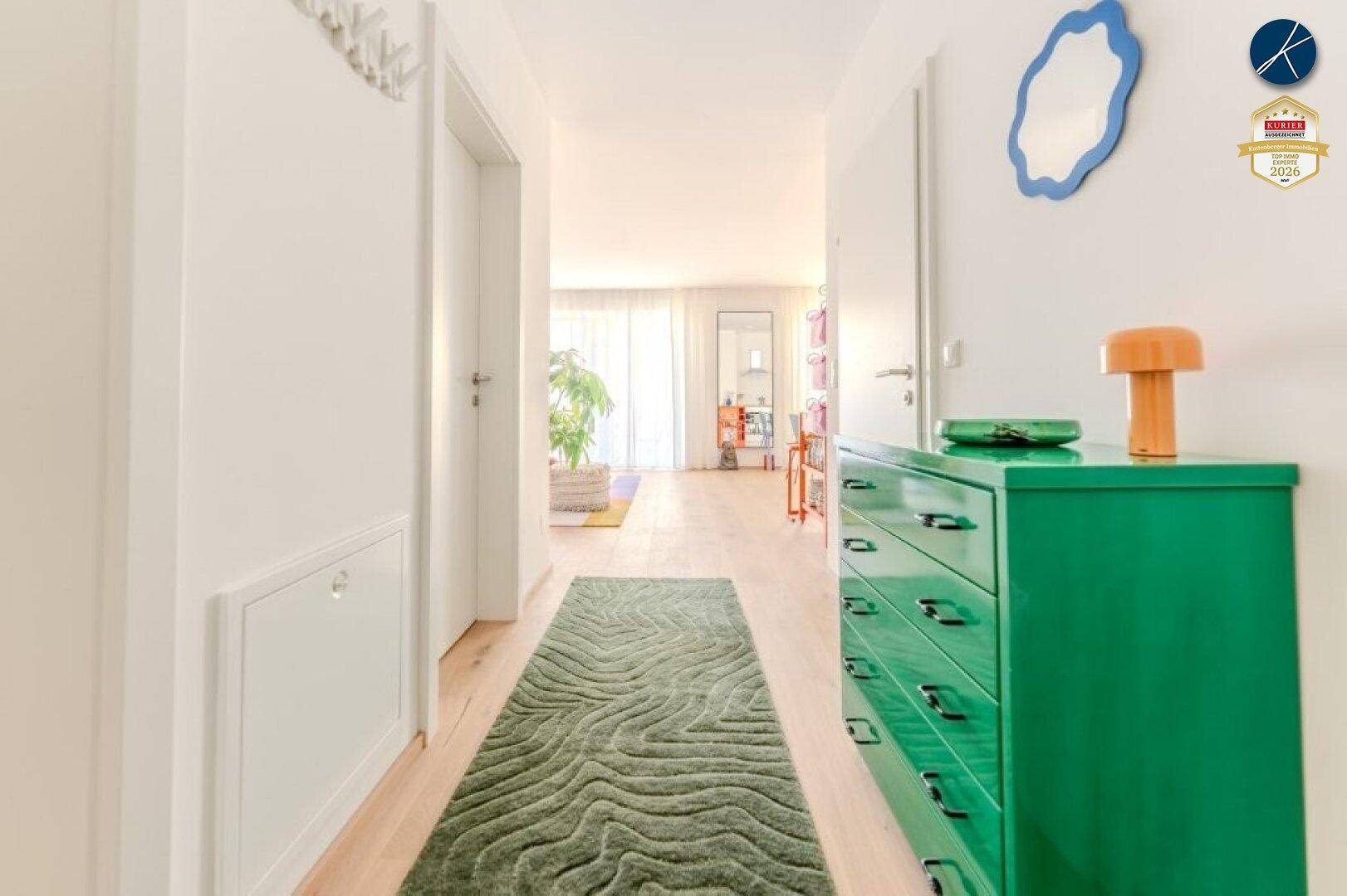 Heller Flur mit grünem Sideboard, modernem Spiegel und Holzboden, der zu den Wohnbereichen führt.
