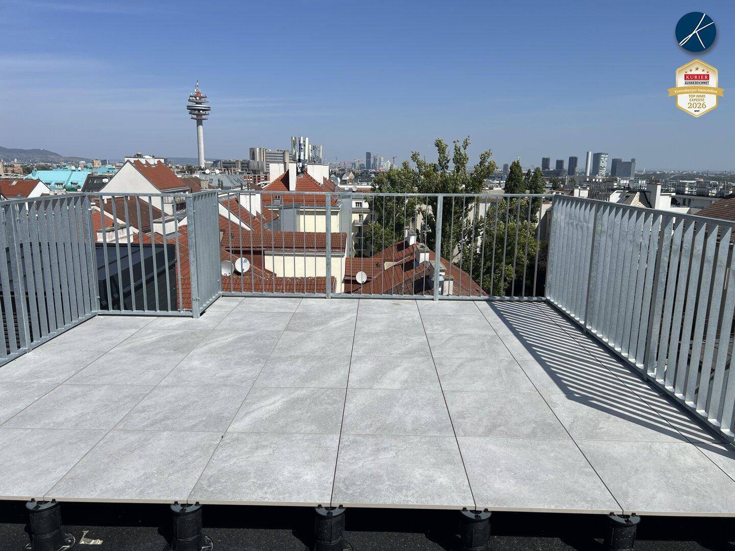 Geräumige Dachterrasse mit Fliesenboden und Metallgeländer, bietet einen weiten Stadtblick.