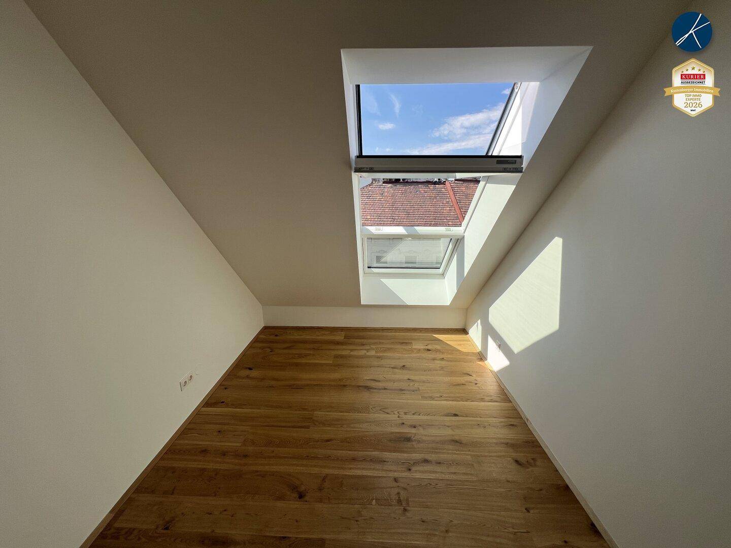 Kleiner, heller Raum im Dachgeschoss mit Holzboden und einem großen Dachfenster.
