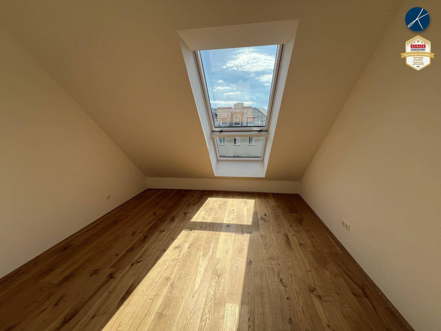 Dachgeschosszimmer mit Holzboden und einem großen Dachfenster, das viel Sonnenlicht spendet.