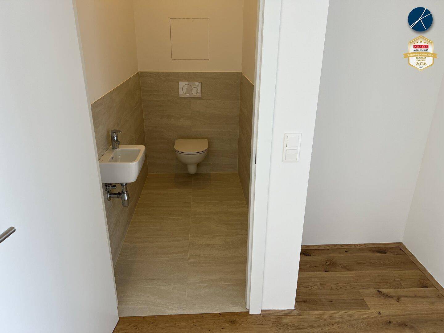 Modernes Gäste-WC mit Wand-WC, kleinem Waschbecken und hellen Fliesen.