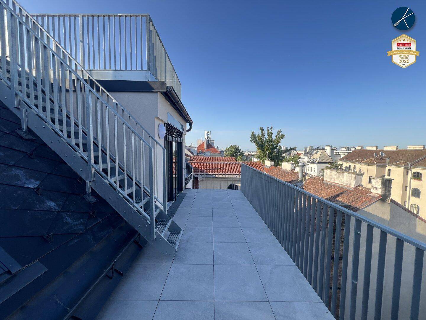 Geräumige Dachterrasse mit Fliesenboden und Metallgeländer, bietet einen weiten Blick über die Stadt.