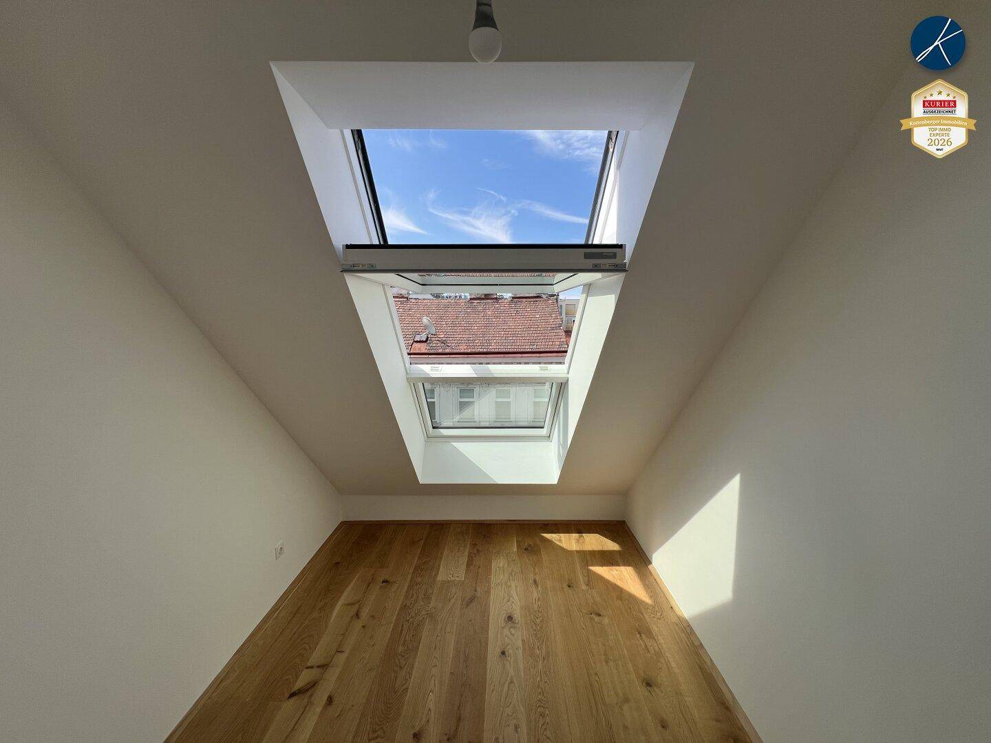 Gemütliches Zimmer mit Holzboden und großem Dachfenster, das viel Tageslicht hereinlässt.