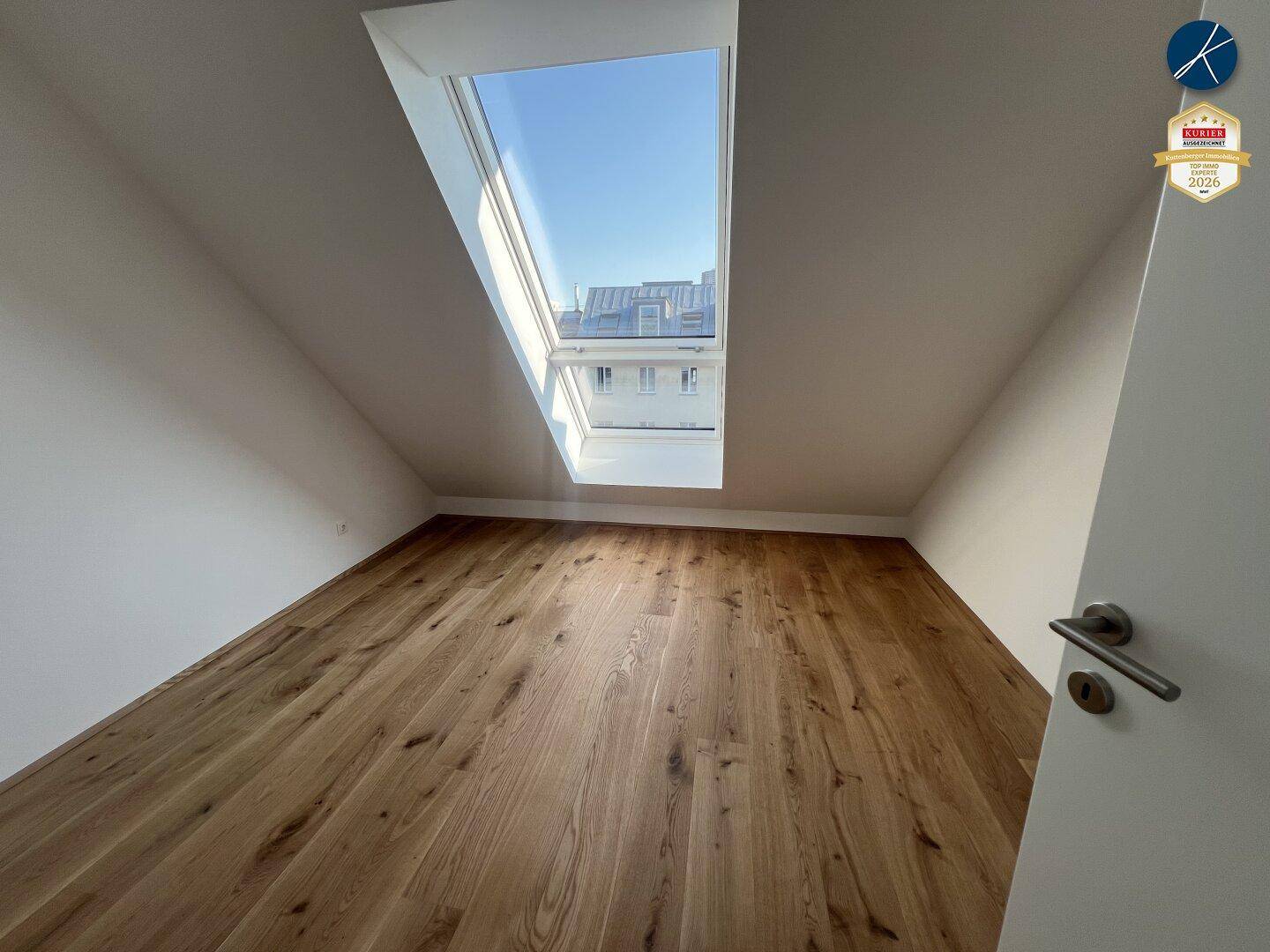Helles Zimmer mit Holzboden und Dachfenster, das viel Tageslicht in den Raum bringt.