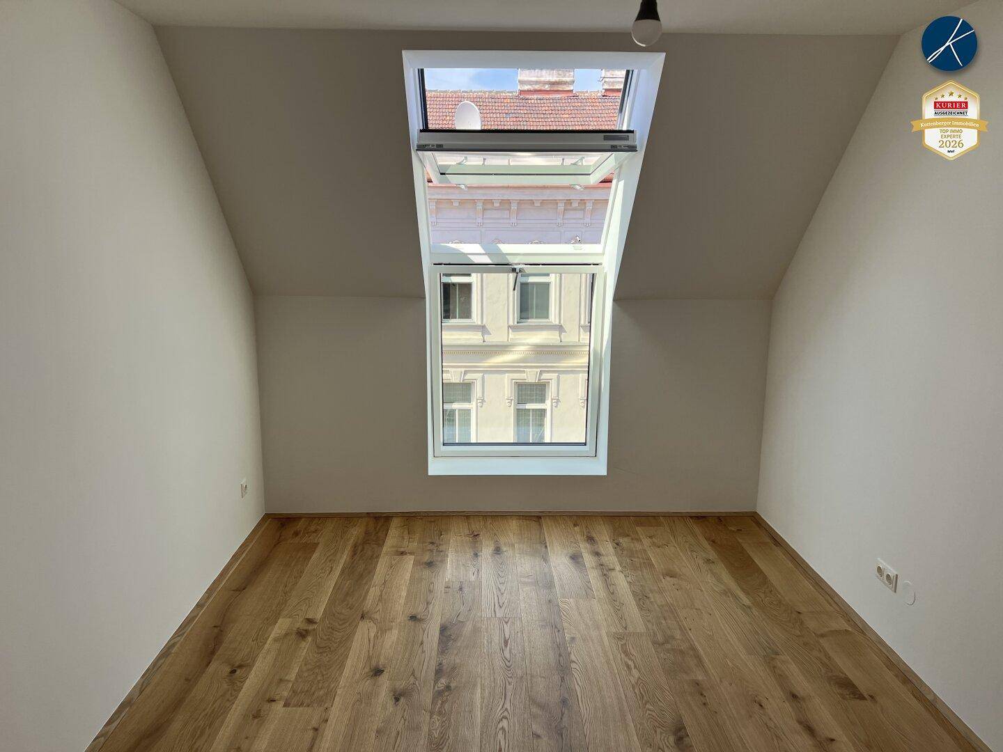 Dachgeschosszimmer mit Holzboden und einem großen, aufklappbaren Dachfenster.
