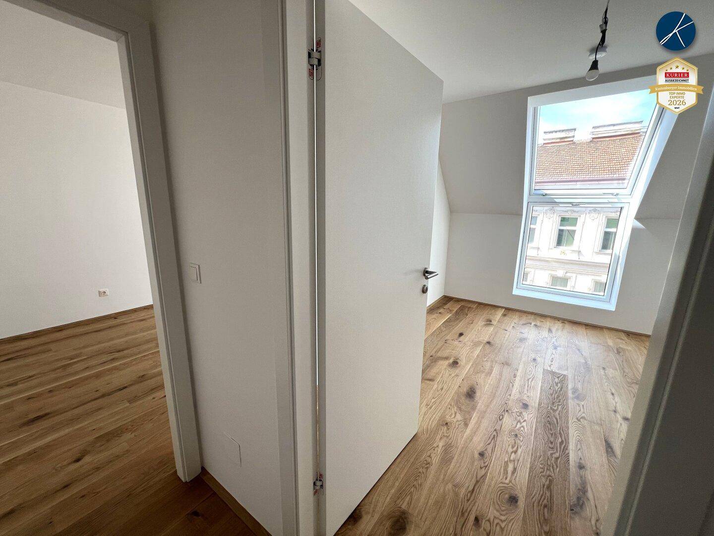Heller Flur mit Holzboden, der zu einem Zimmer mit Dachfenster führt.