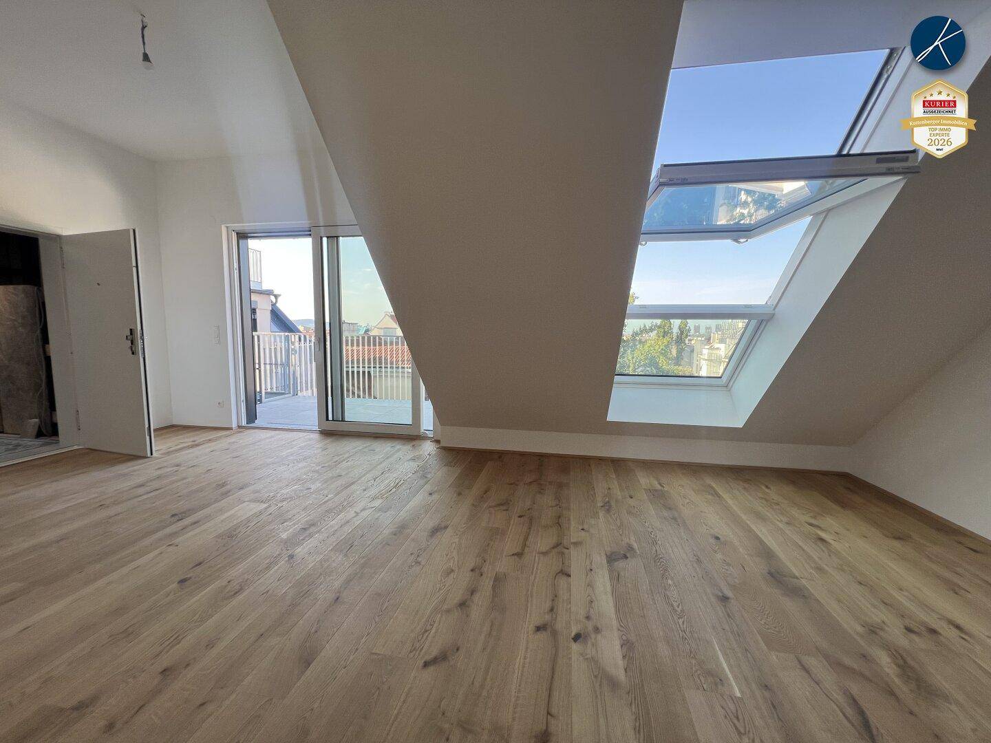Heller Raum mit Holzboden, Zugang zu einem Balkon und großen Dachfenstern.