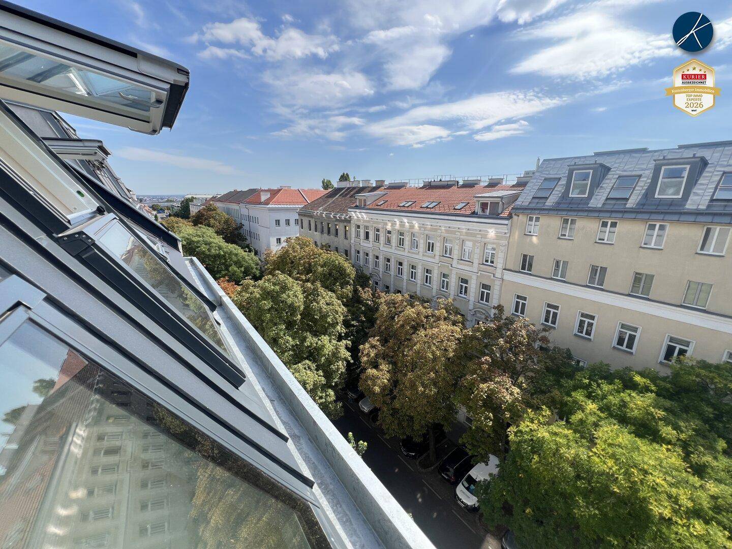 Weitblick über die Stadt mit grünen Baumkronen und moderner Dacharchitektur unter blauem Himmel.
