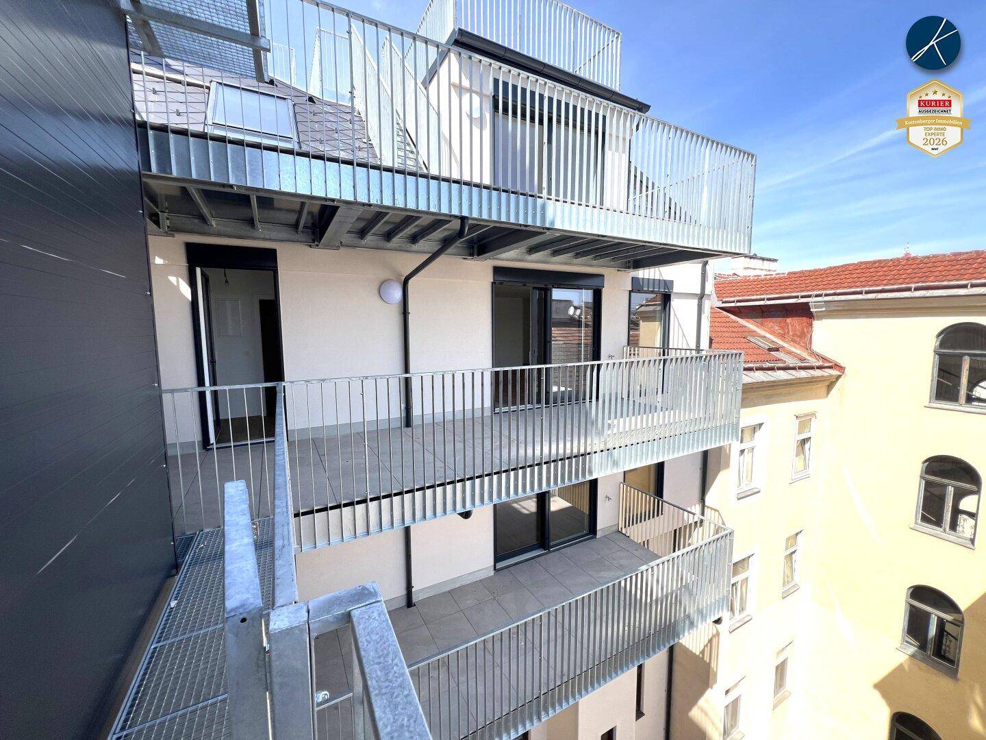 Mehrere moderne Balkone und eine Dachterrasse mit Metallgeländern an einer neuwertigen Gebäudefassade.