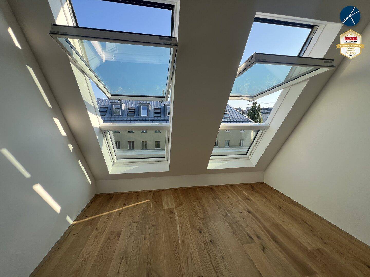 Heller Dachgeschossraum mit Holzboden und zwei großen Dachfenstern, die den Raum erhellen.